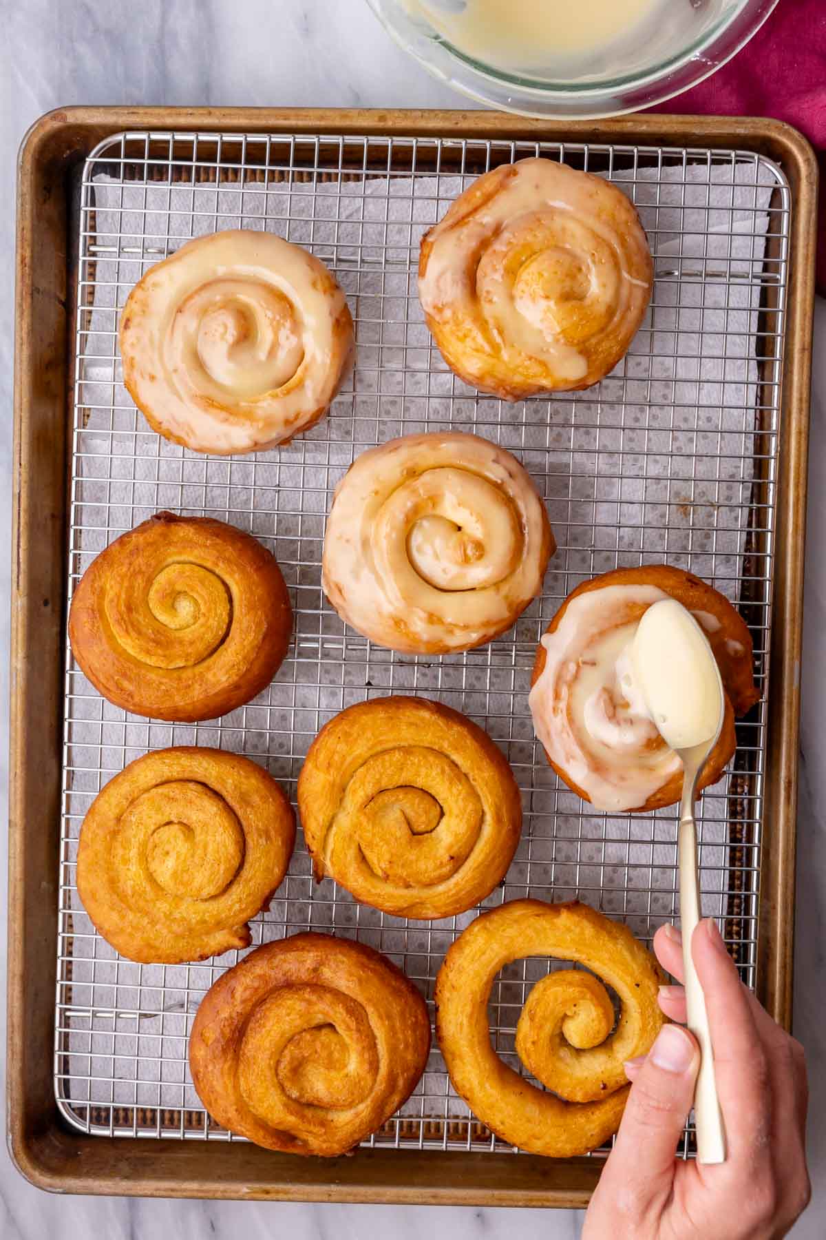 Spooning glaze over golden brown buns made with honey, cinnamon, and sugar.