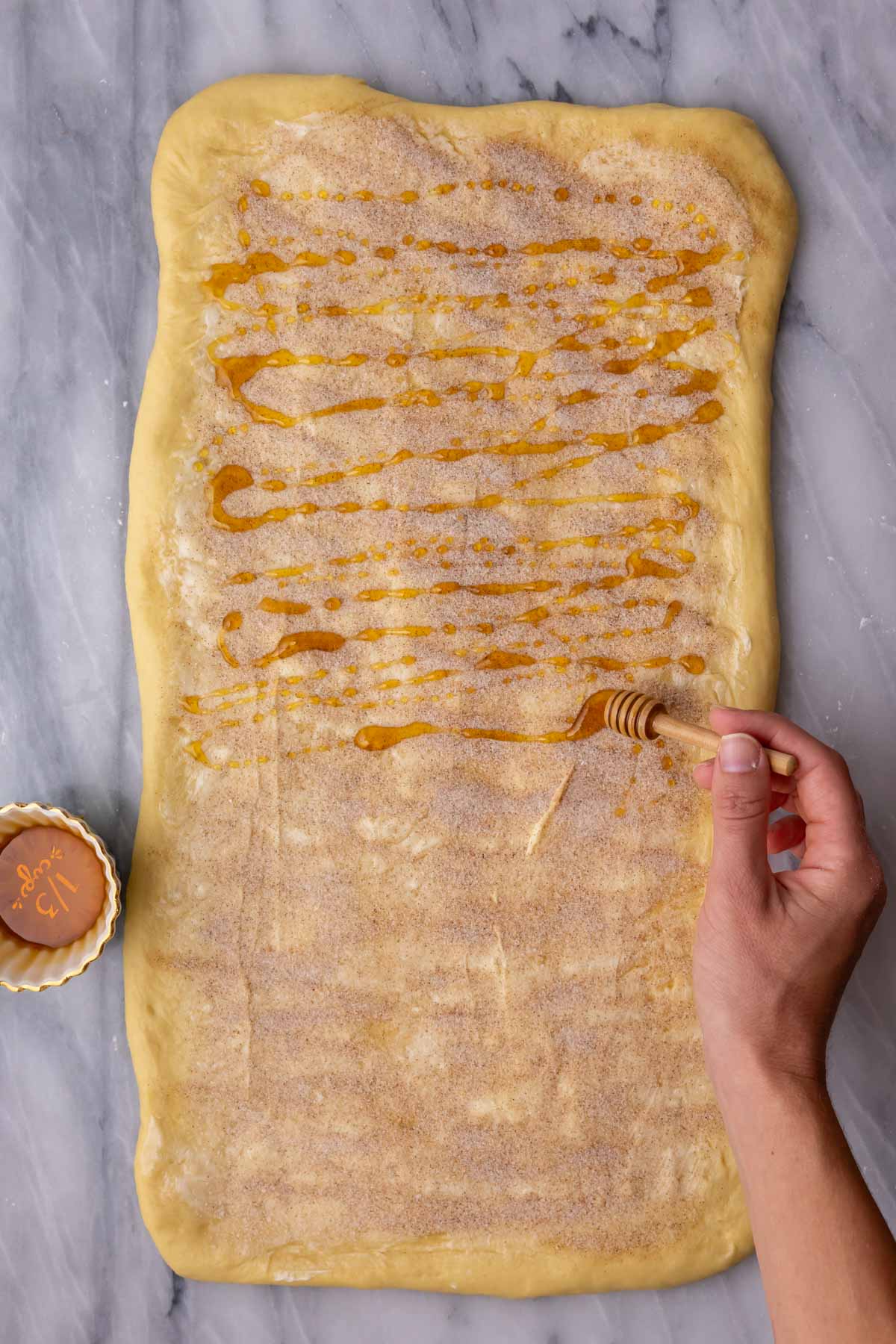 Drizzling honey over butter, cinnamon, and sugar on a rectangular portion of dough.