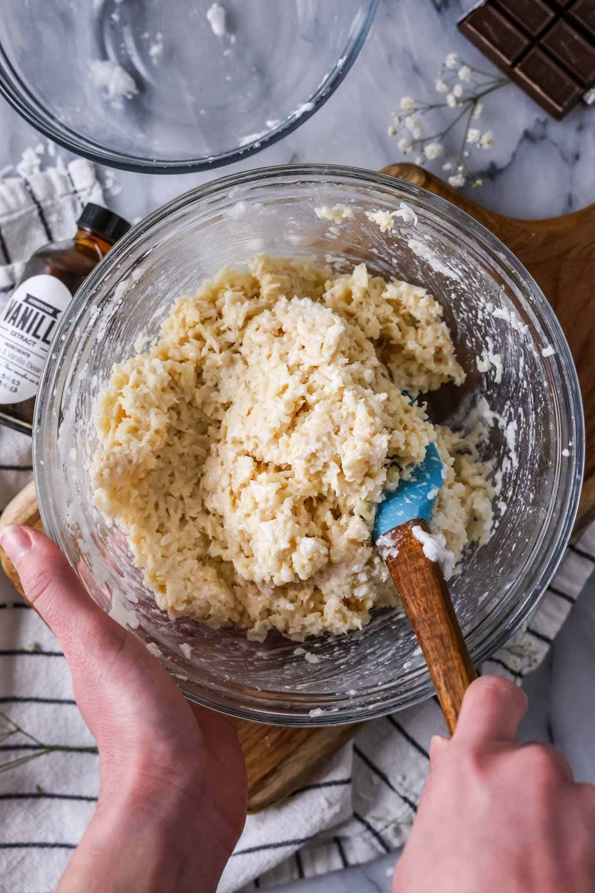 Overhead view of a bowl of coconut being stirred together with whipped egg whites and condensed milk for macaroons.