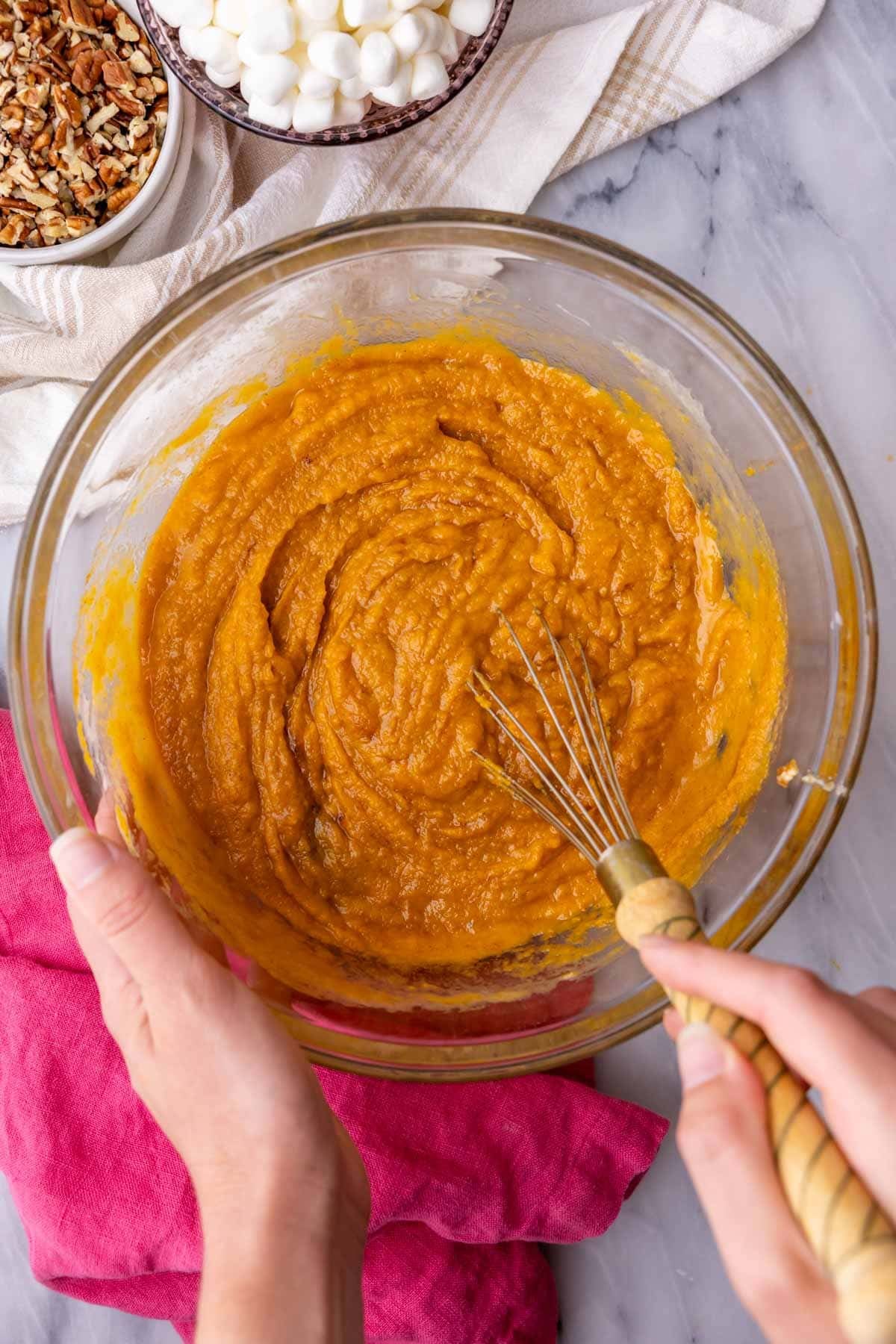 Mixing together all the filling ingredients for sweet potato casserole with a whisk in a clear mixing bowl.