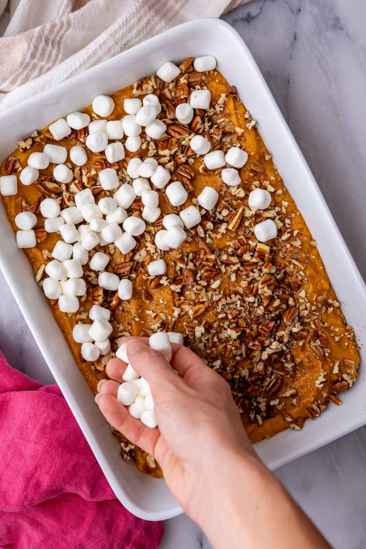 Scattering marshmallows and pecans over the unbaked sweet potato casserole.