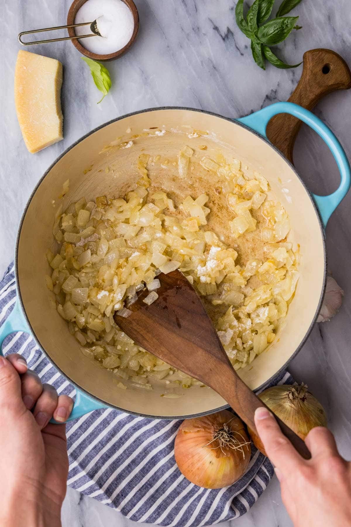 Stirring flour into cooked, diced yellow onions in a large blue pot.
