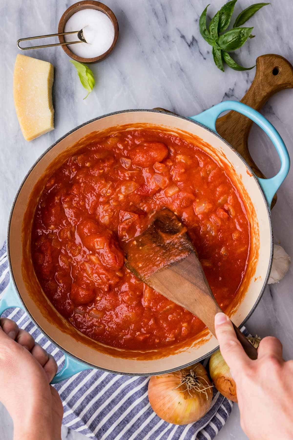 Wooden spoon breaking up whole peeled tomatoes in pot to make tomato soup. 