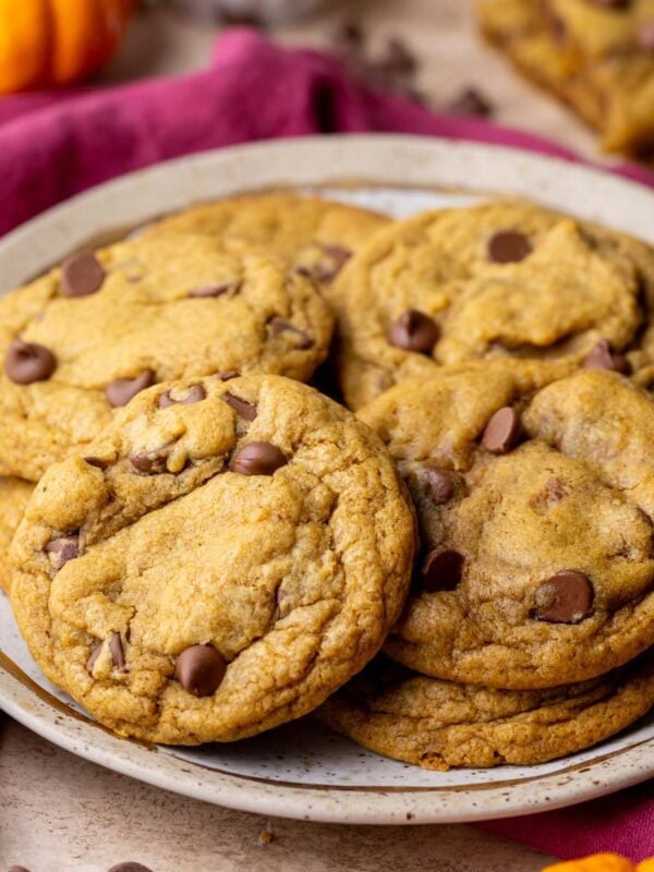 A plate full of chewy pumpkin chocolate chip cookies with pumpkins in the foreground and background.