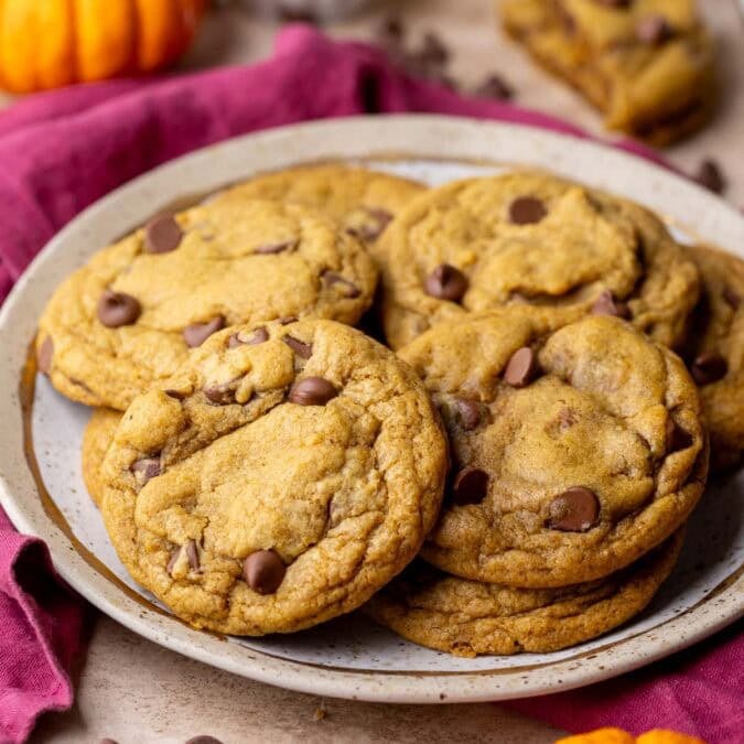 A plate full of chewy pumpkin chocolate chip cookies with pumpkins in the foreground and background.