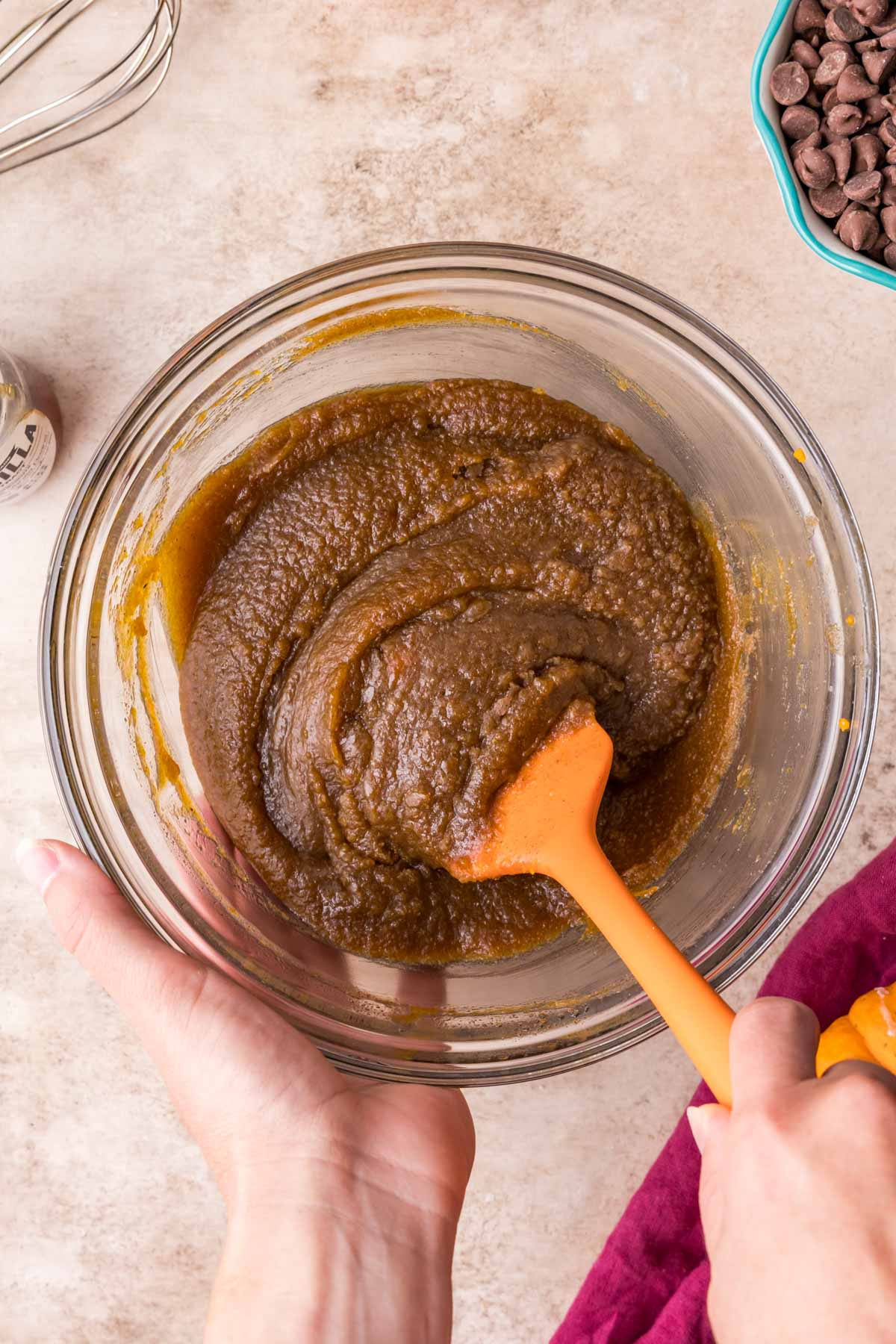 Using an orange spatula to stir together the wet ingredients and sugar to make cookie dough.
