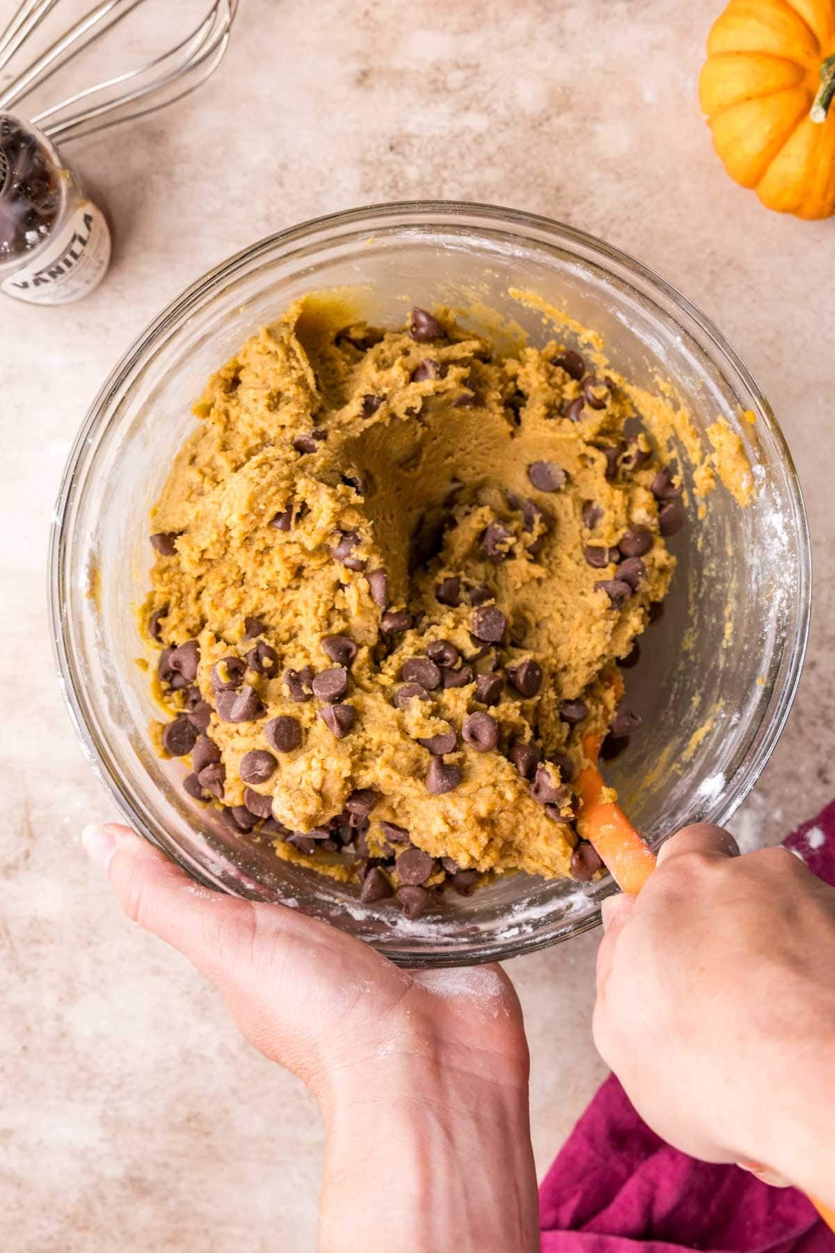 Stirring milk chocolate chips into pumpkin cookie batter in a glass bowl.