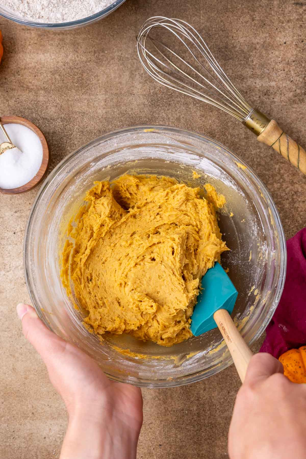 Overhead view of a bowl of soft and cakey pumpkin cookie dough being stirred with a spatula.