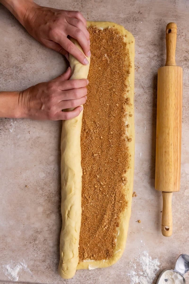 Rolling a dough log filled with cinnamon and sugar.
