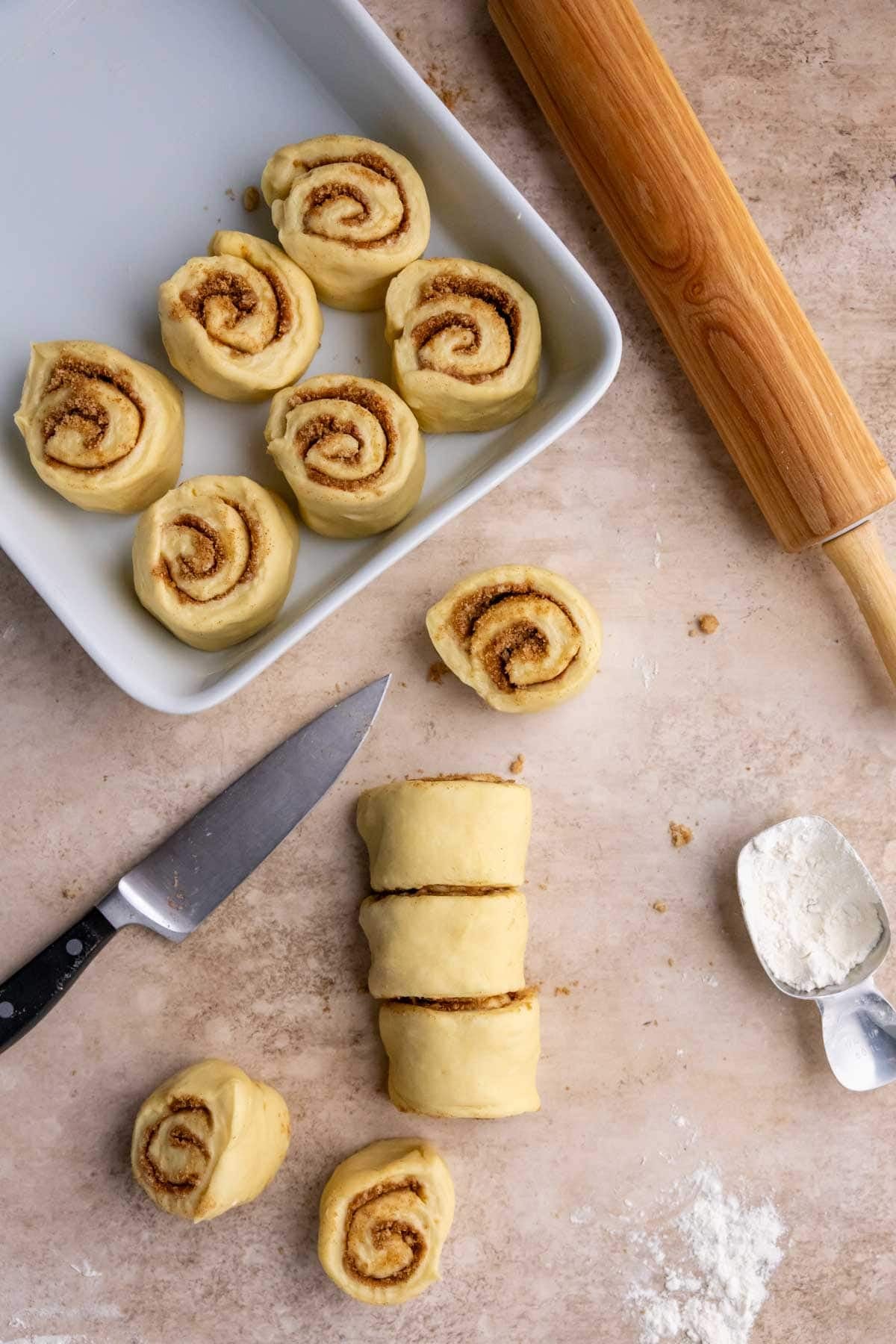 Cinnamon rolls being cut and arranged in a baking dish.