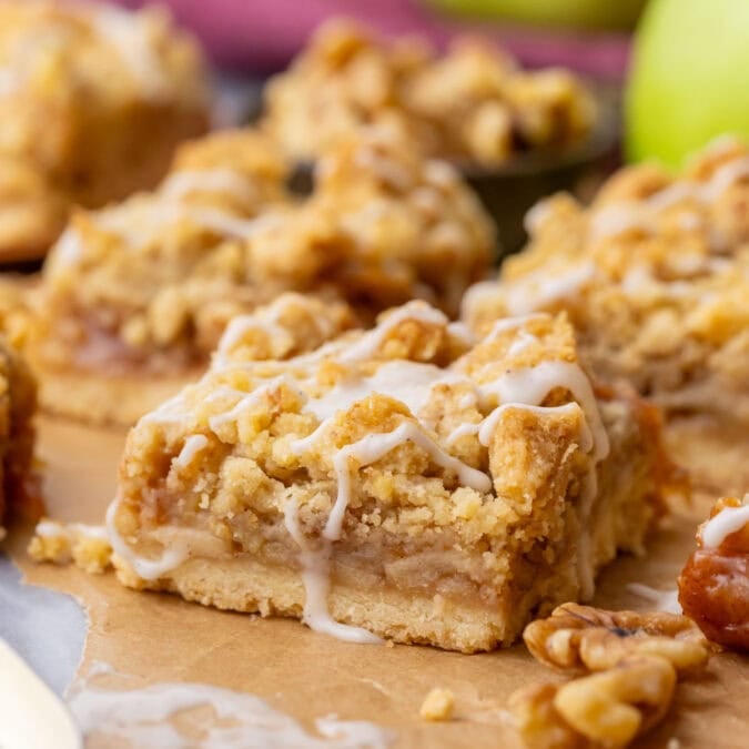 Close-up of apple pie bars made with a shortbread crust, apple filling, crumb topping, and vanilla glaze drizzle.