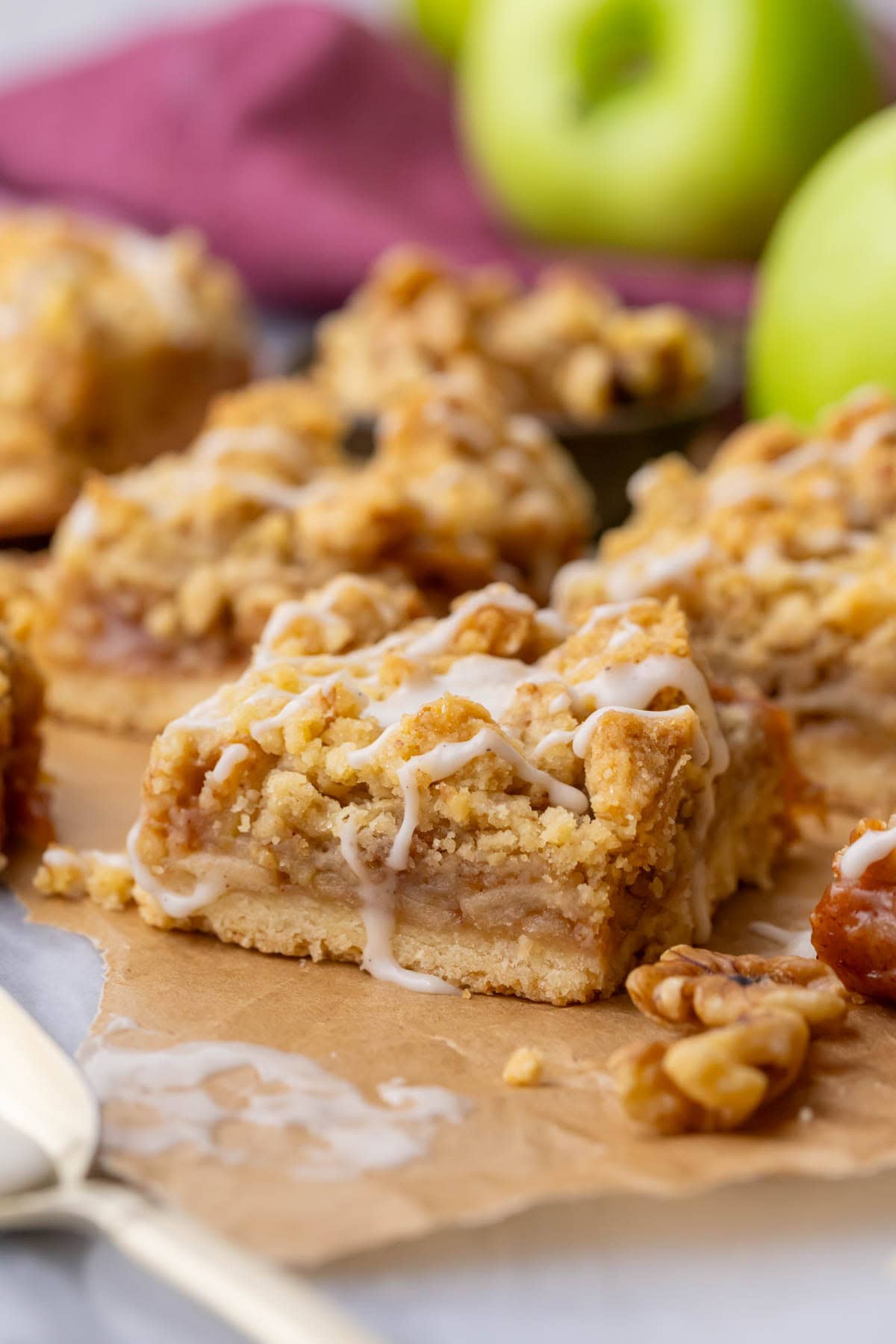 Close-up of apple pie bars made with a shortbread crust, apple filling, crumb topping, and vanilla glaze drizzle.