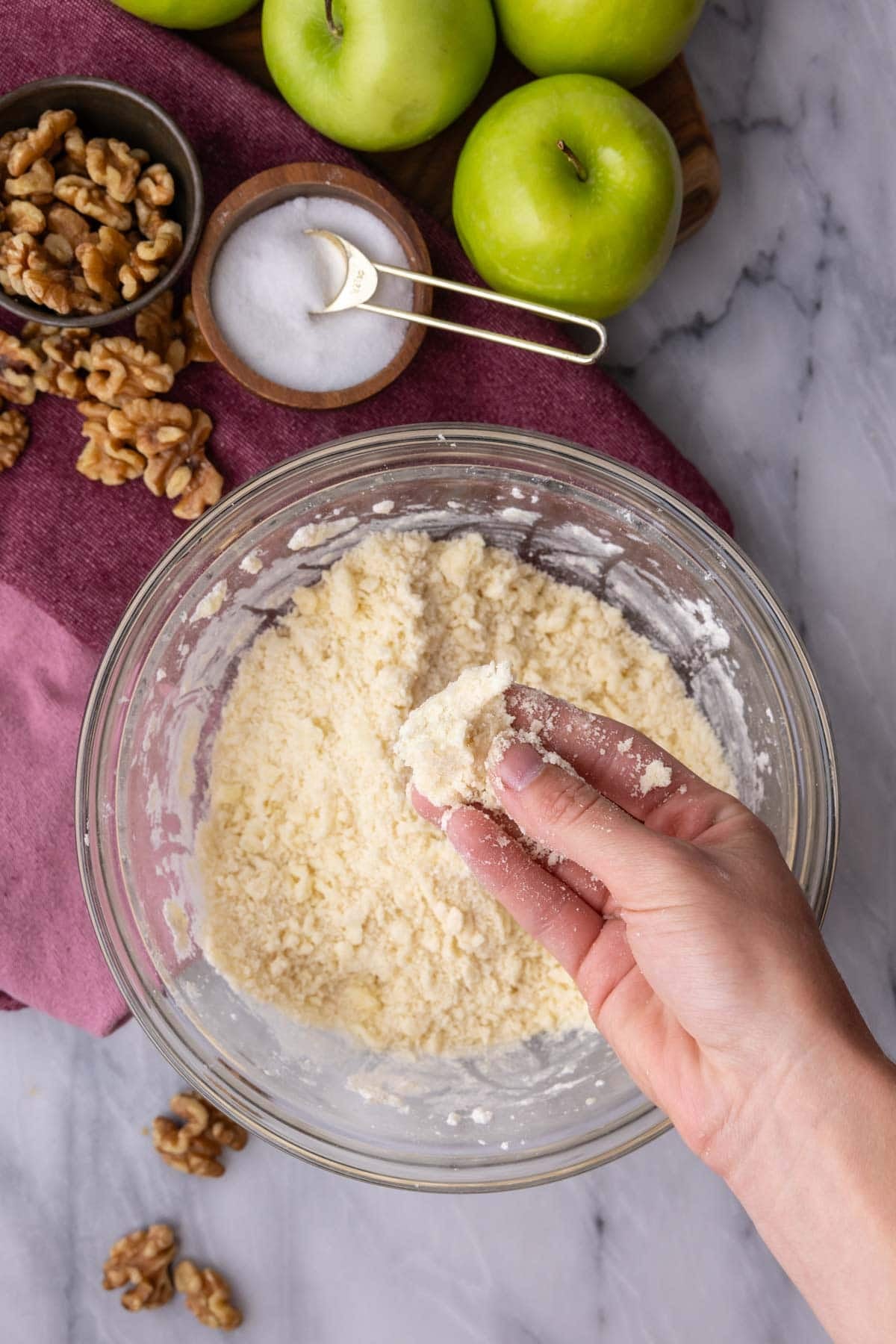 Overhead view of hands pinching together a sandy mixture in a bowl.