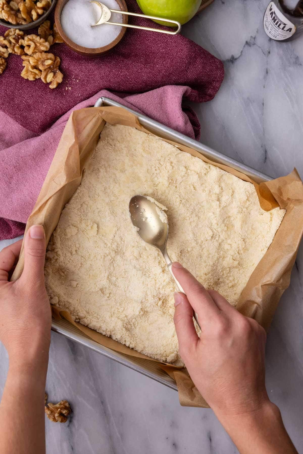 Spoon pressing a crust into a parchment lined pan.