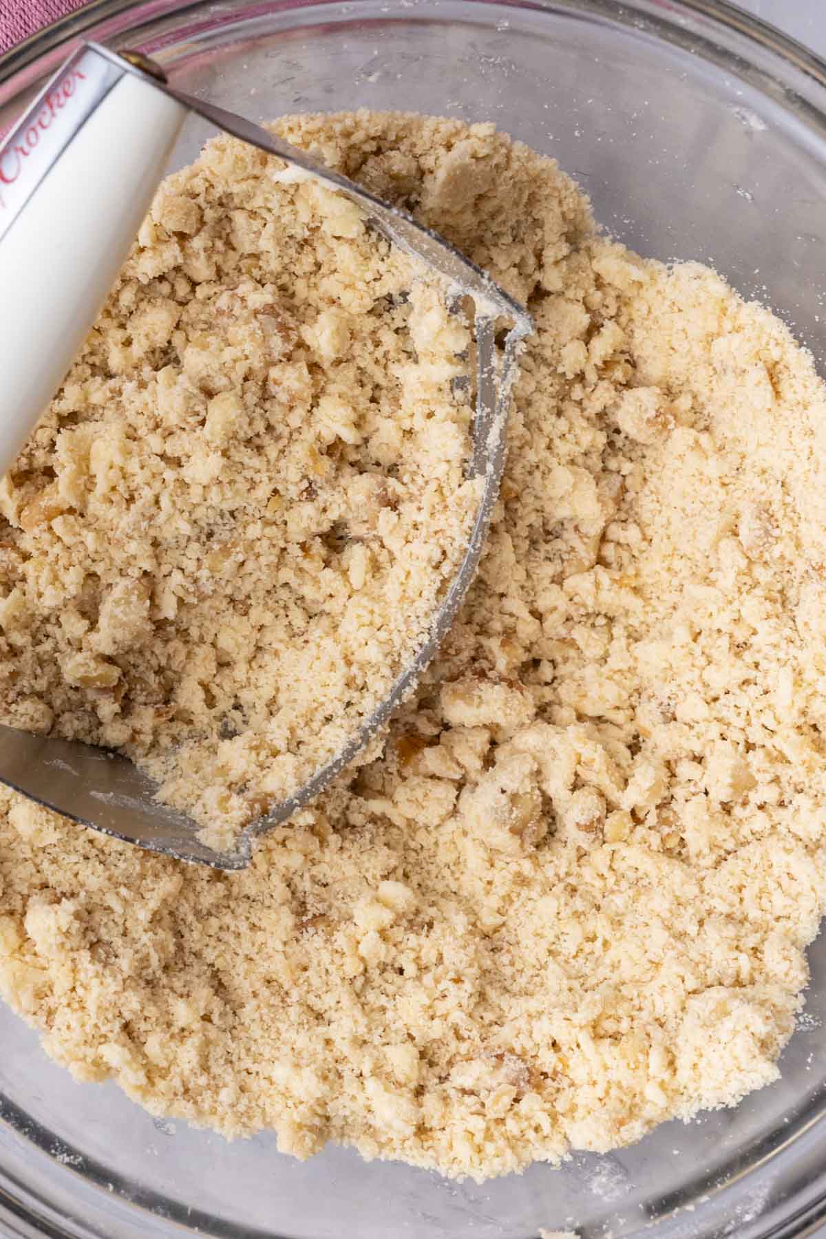 Pastry cutter resting in a bowl of a crumbly mixture.