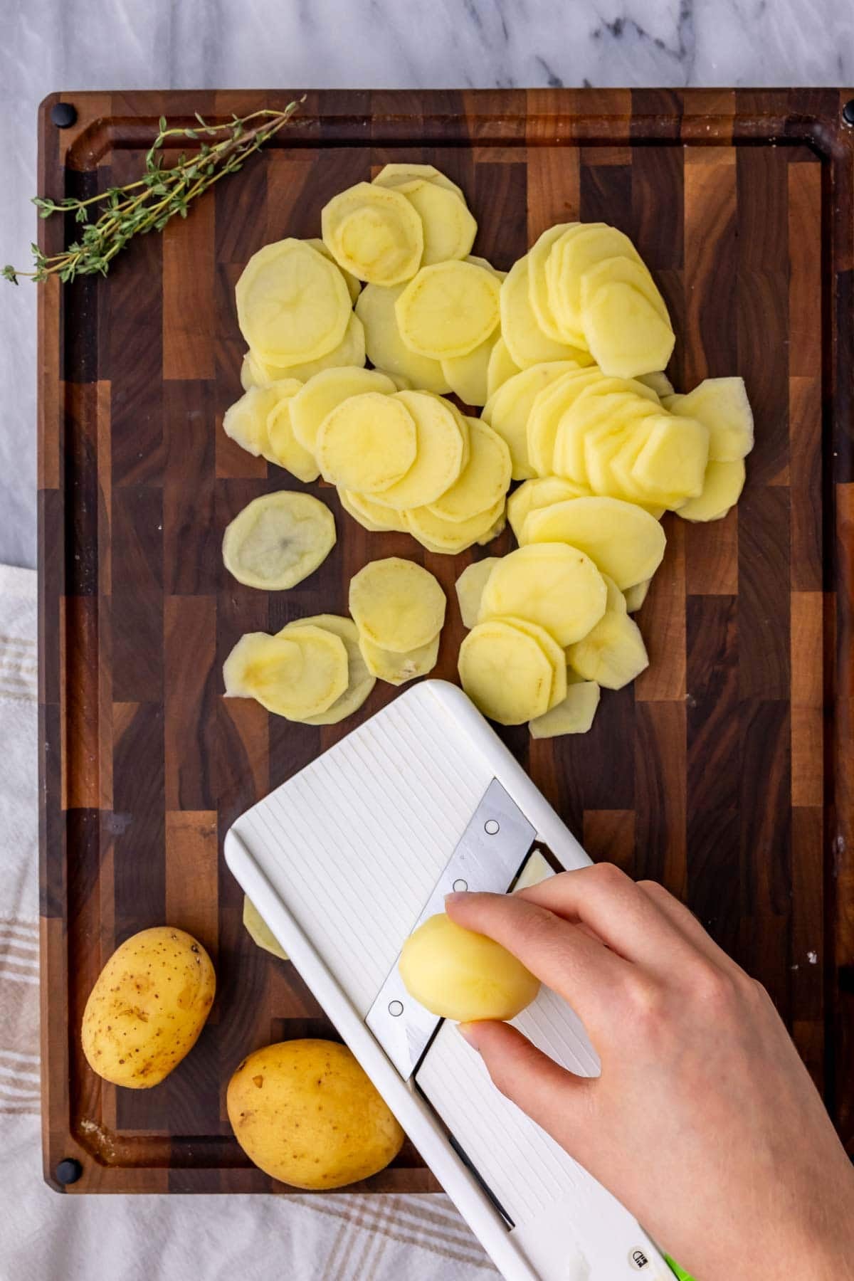 Overhead view of potatoes being sliced into thin rounds with a mandolin.