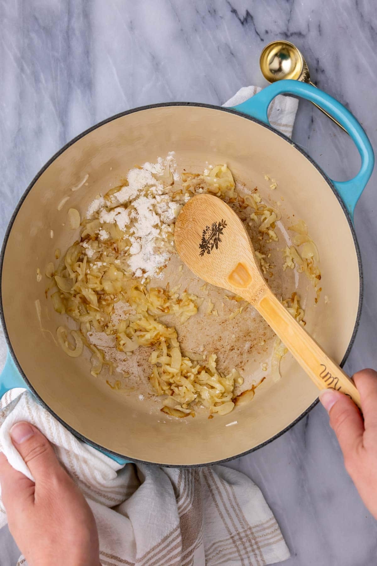 Overhead view of flour being stirred into caramelized onions in a dutch oven.