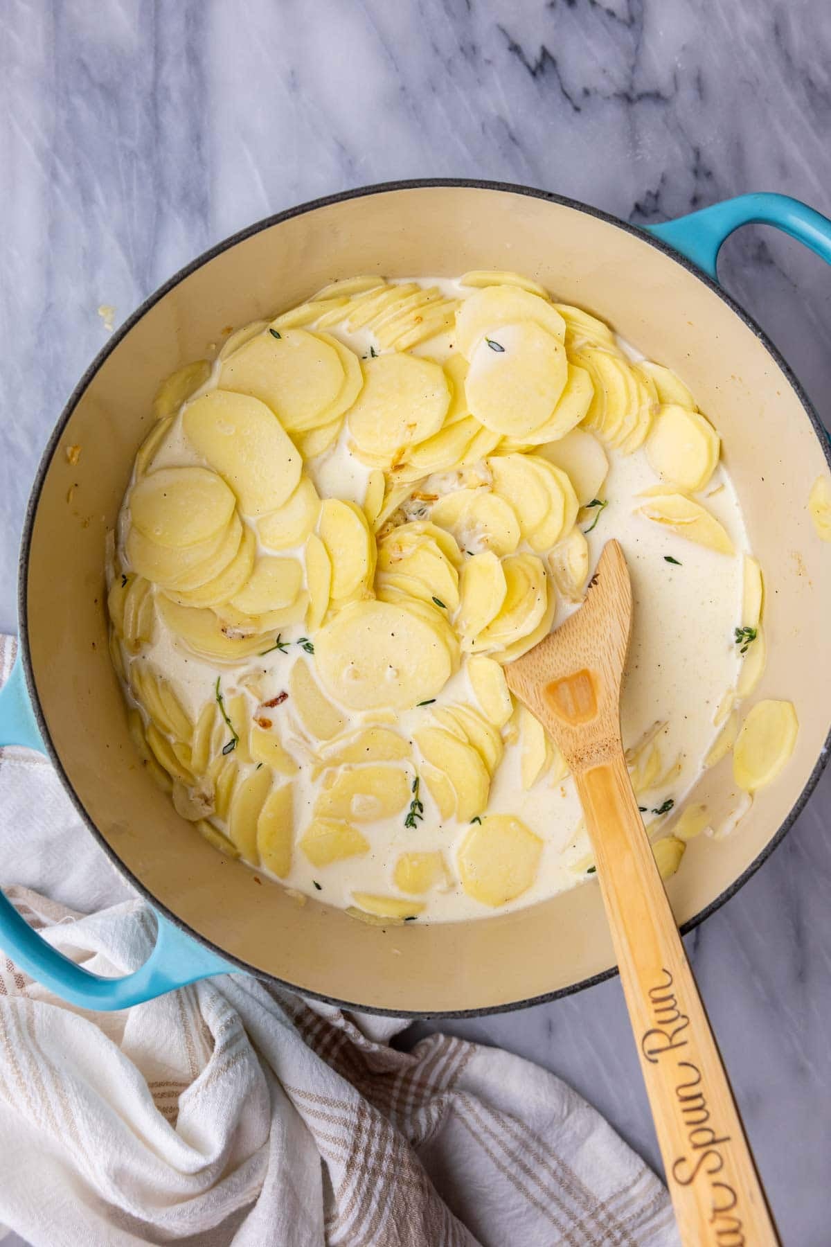 Overhead view of a Dutch oven with sliced potatoes, milk, cream, and spices.