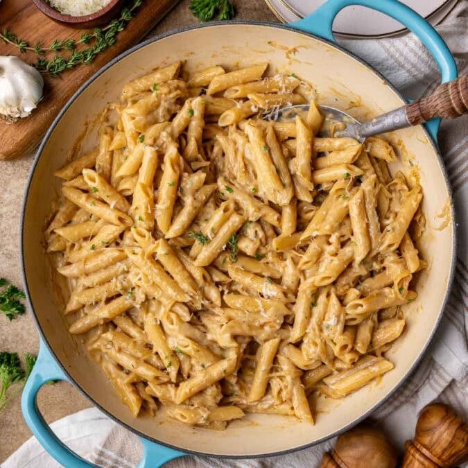 Overhead view of a skillet of French onion pasta topped with fresh parsley and parmesan.