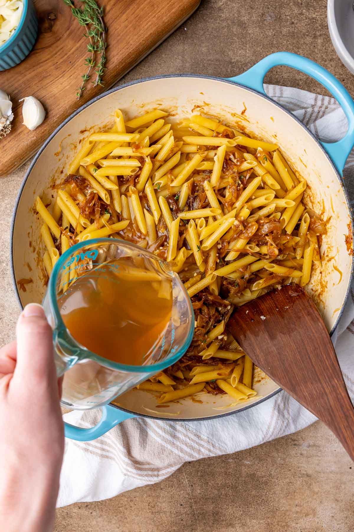 Pouring beef broth into a skillet of pasta and caramelized onions.