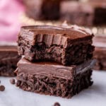 Two fudge frosted brownies stacked on top of each other with the top brownie missing a bite.