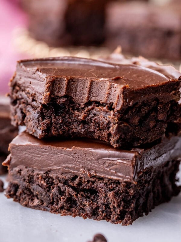 Two fudge frosted brownies stacked on top of each other with the top brownie missing a bite.
