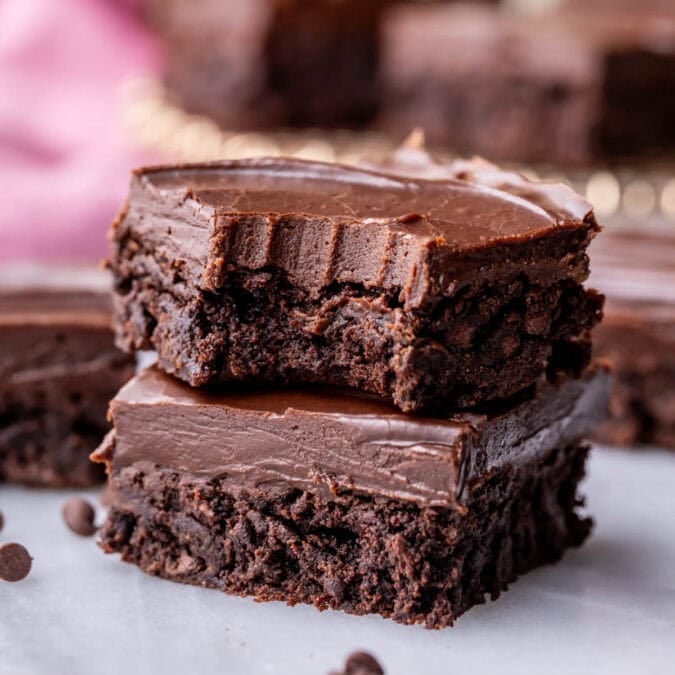 Two fudge frosted brownies stacked on top of each other with the top brownie missing a bite.