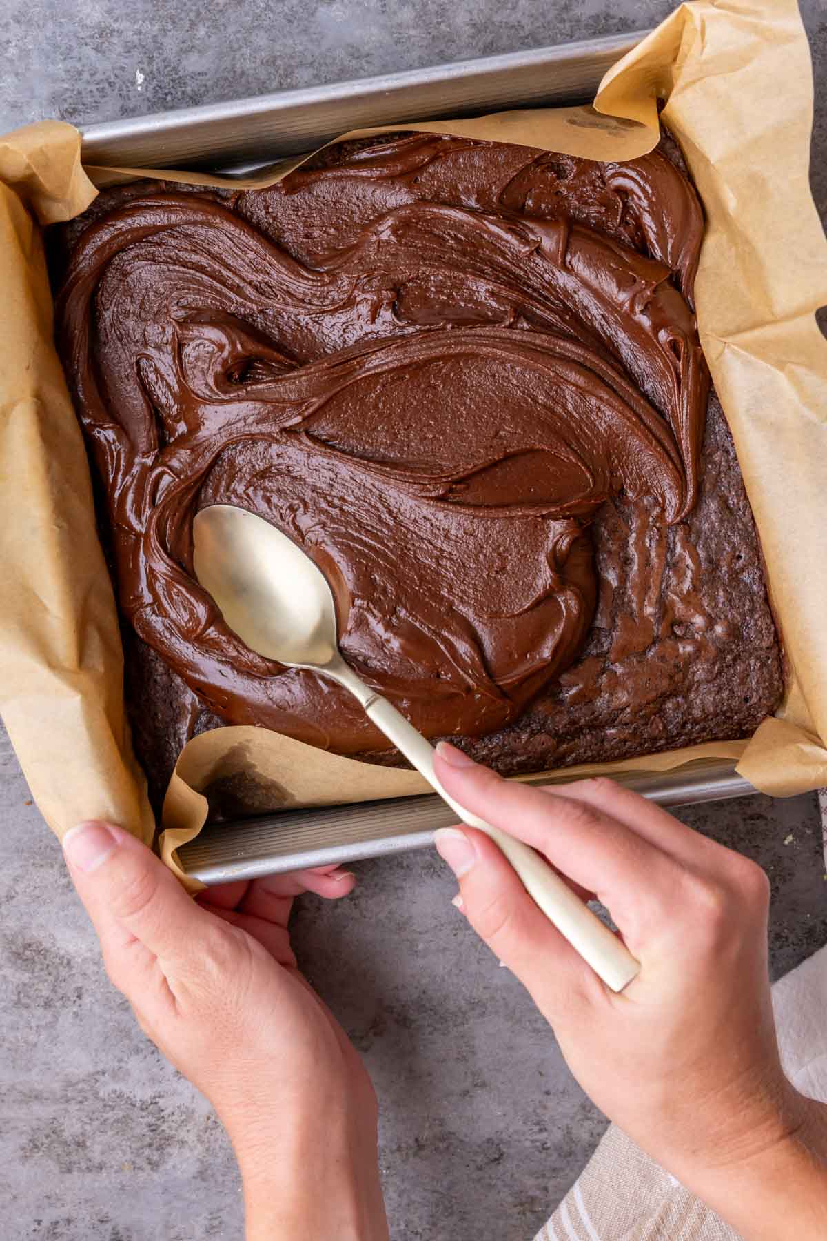Overhead view of fudge frosting being smoothed over brownies with a spoon.
