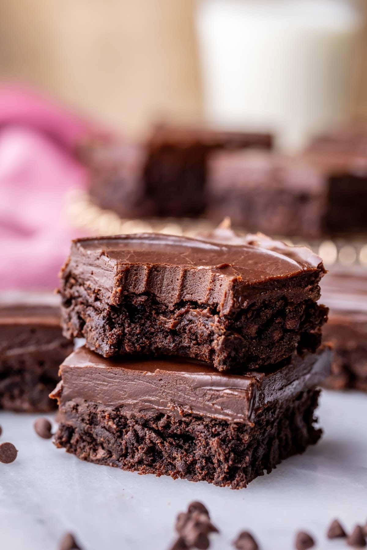 Two fudge frosted brownies stacked on top of each other with the top brownie missing a bite.