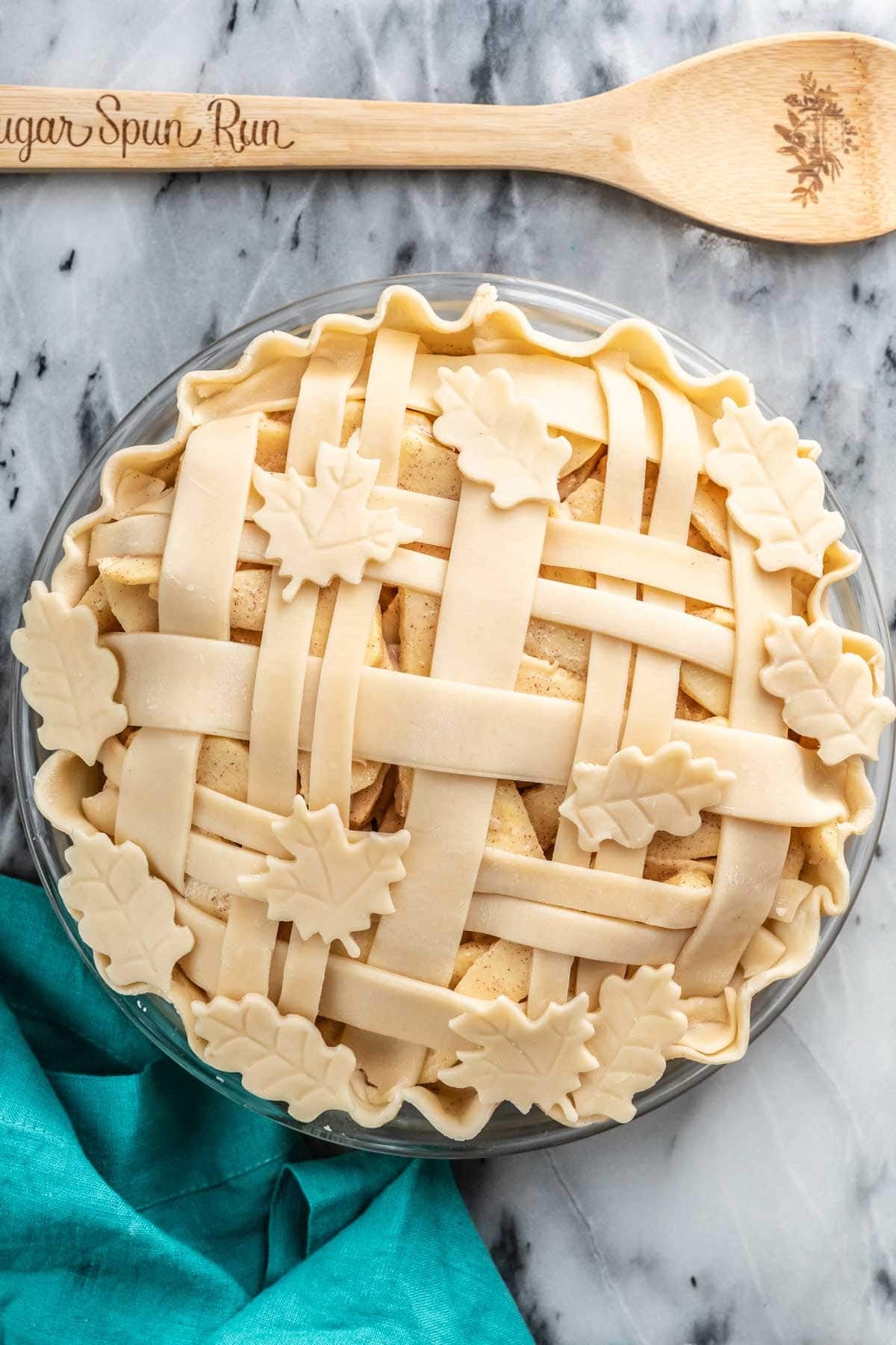 Overhead view of a woven pie crust topped with leaf shaped pie dough pieces before baking.