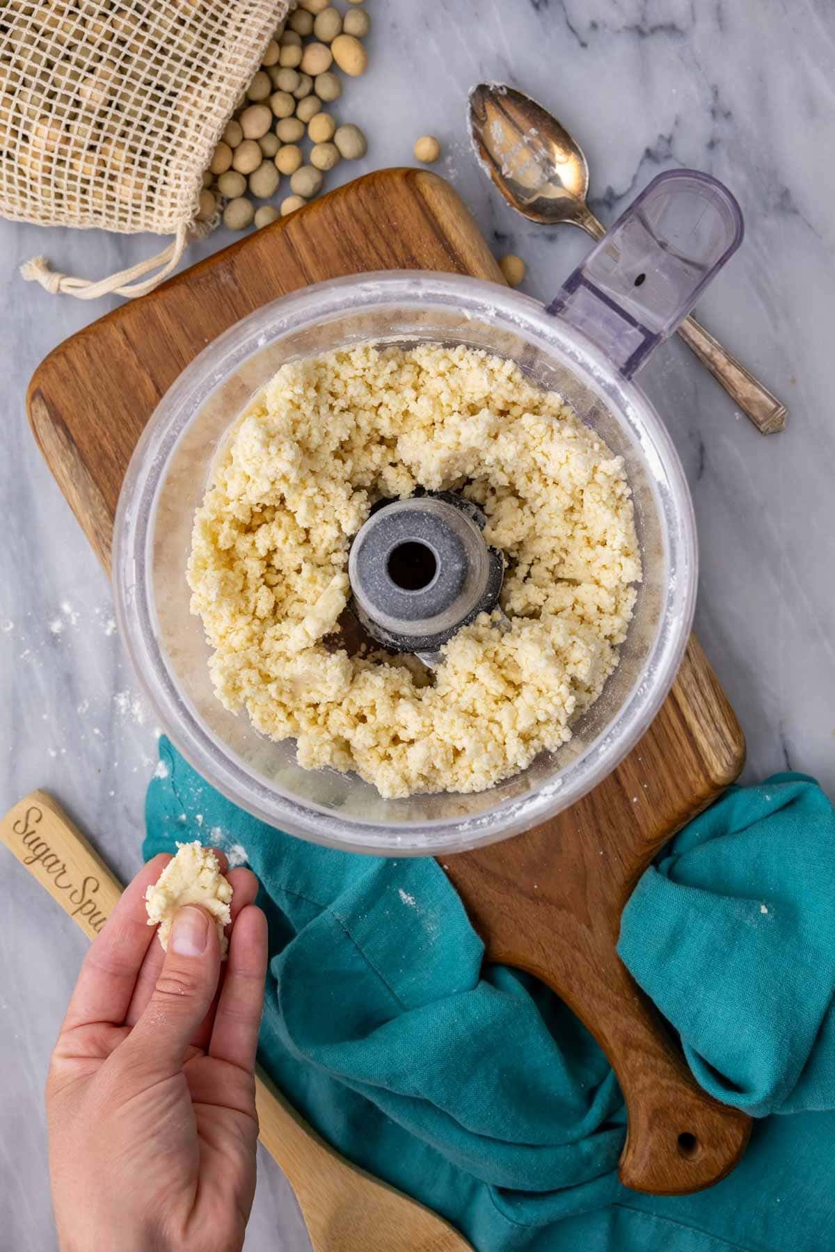 Overhead view of a crumbly pie dough in a food processor bowl that stays together when pinched.